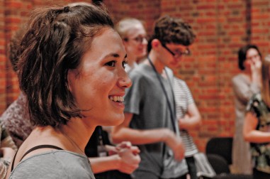 a young female composer smiling, other people are out of focus in the background